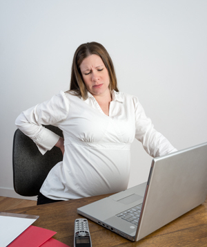 Pregnant Woman Stretching Her Aching Back Sitting At A Desk